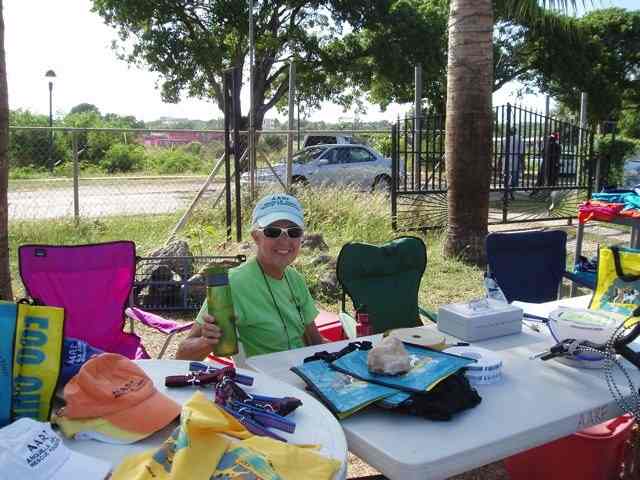 In this photo, Althea sits at the AARF table which displays many items for sale, such as shirts, hats, collars. leashes, beverage bags and more
